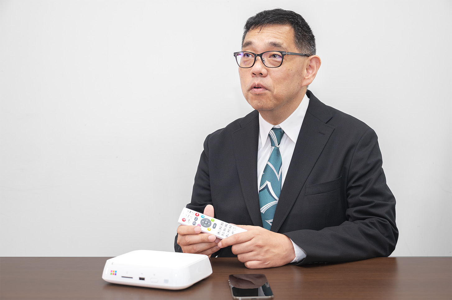 おもいでばこ本体とリモコンを前に、デジカメのHEIF対応やHDR表示改善を解説する根本氏